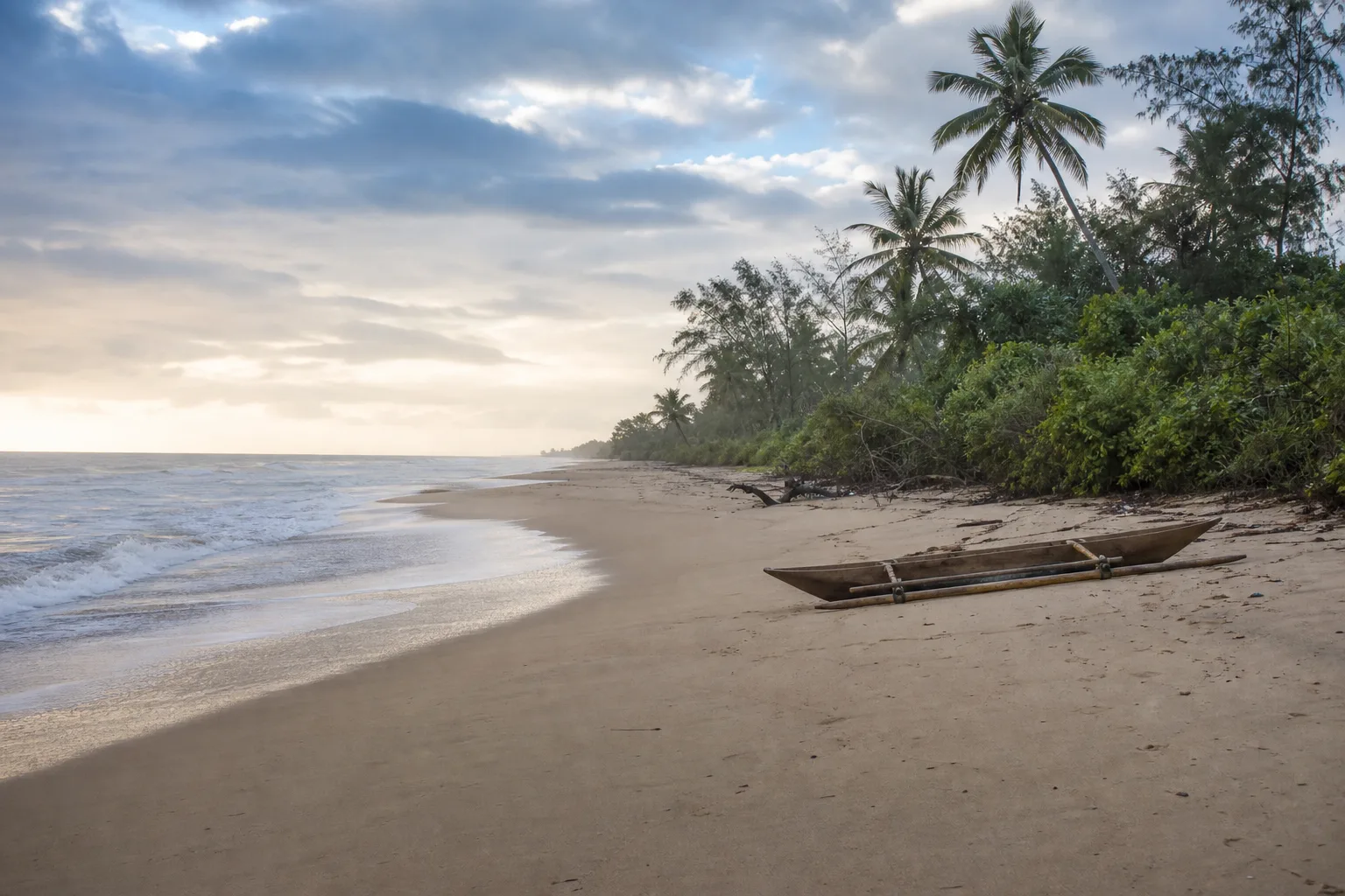 Littoral sableux bordé de végétation avec une pirogue sur le rivage